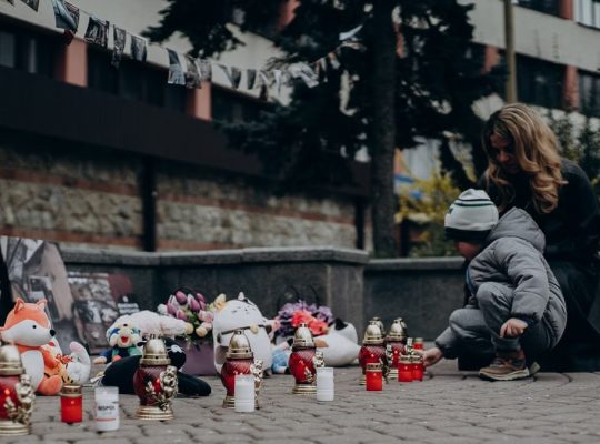 Mother and child paying tribute with candles and gifts at a memorial in Ukraine, showcasing remembrance and emotional connection.