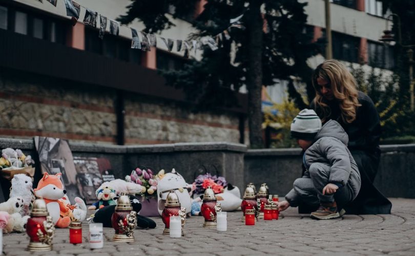 Mother and child paying tribute with candles and gifts at a memorial in Ukraine, showcasing remembrance and emotional connection.