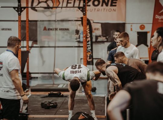 Group of athletes engaging in a competitive CrossFit workout at a gym with emphasis on strength and teamwork.