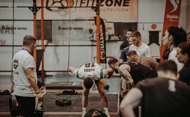 Group of athletes engaging in a competitive CrossFit workout at a gym with emphasis on strength and teamwork.